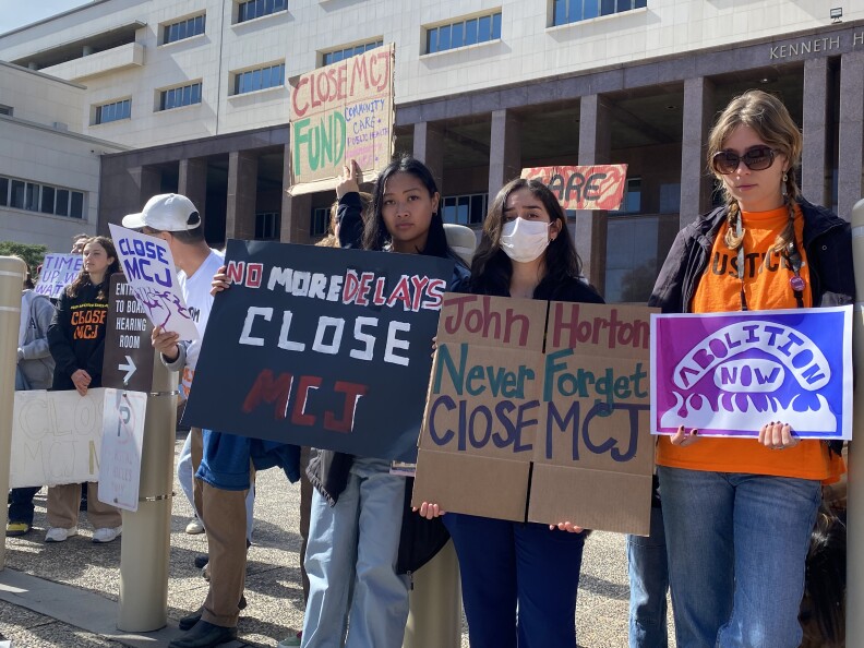  Protesters hold signs which read: "No More Delays: Close MCJ" and "John Horton: Never Forget: Close MCJ" 