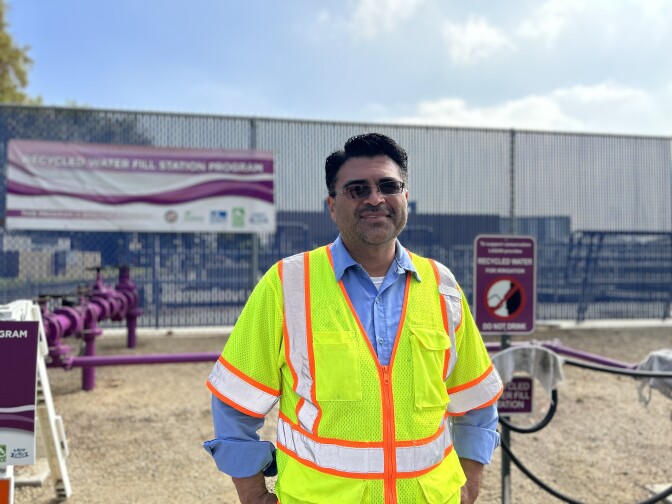 A man in a bright yellow vest smiles at the camera while standing by the fill station.