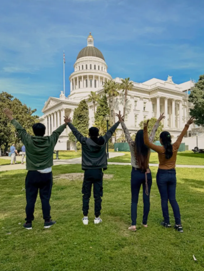 Four teens are standing on a lawn outside the state Capitol. 