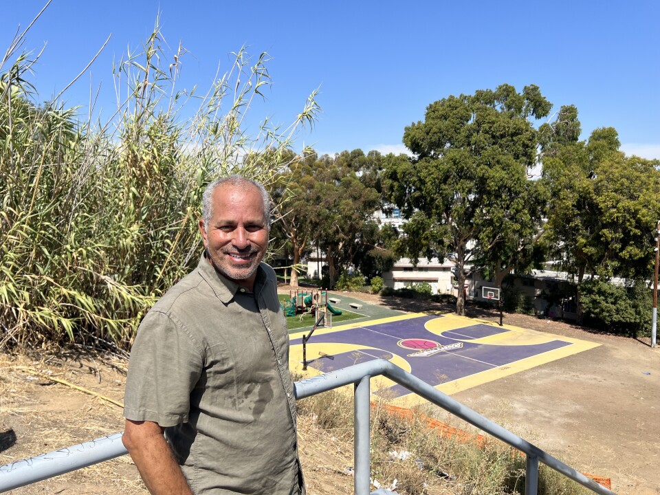 A Brown man in a green shirt stands near a basketball court of the Ramona Gardens housing development.