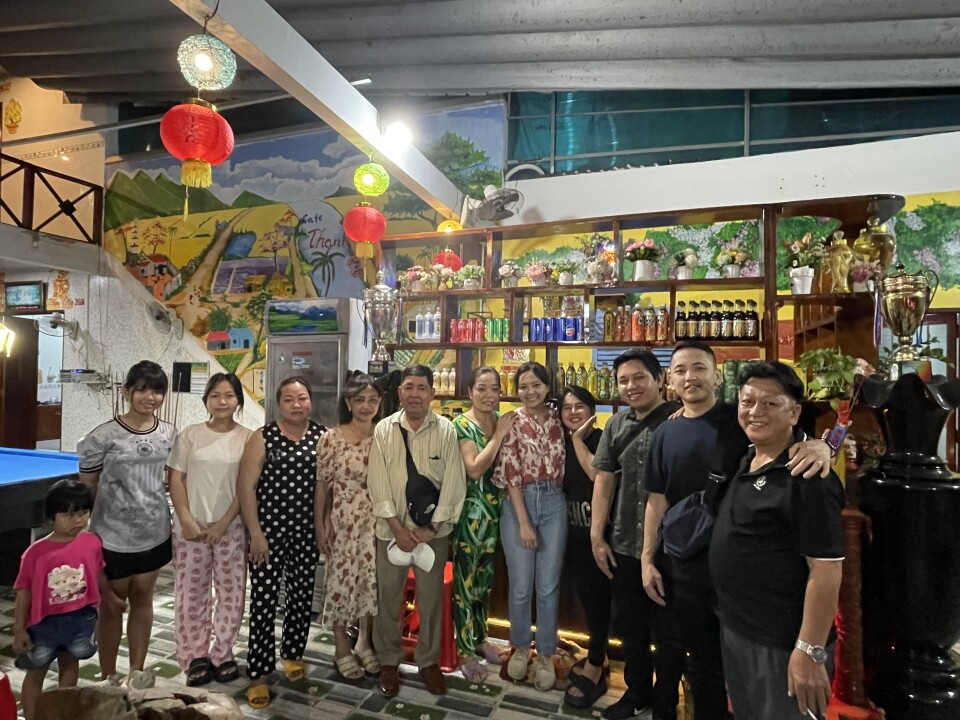 A group of people stand in front of a bar displaying different drinks. 