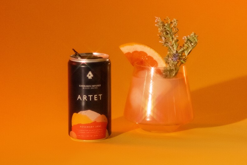 a small black can next to a glass filled with orange liquid and topped with a grapefruit wedge and a sprig of some sort of herb