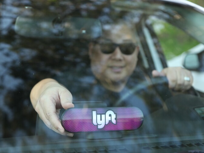 A Lyft driver places a company emblem on his dashboard Jan. 31, in San Francisco. Lyft announced it's offering education benefits, a move aimed at recruiting and retaining drivers in its competition with Uber.