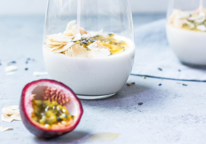 a sliced open passion fruit sits on a counter next to a glass of plain yogurt