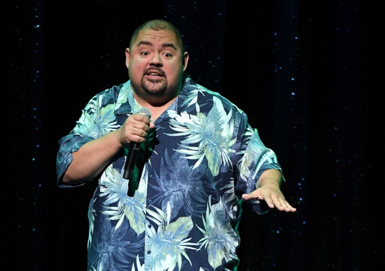 Gabriel Iglesias in a flowery Hawaiian shirt in blues and greens with a mic in his right hand.