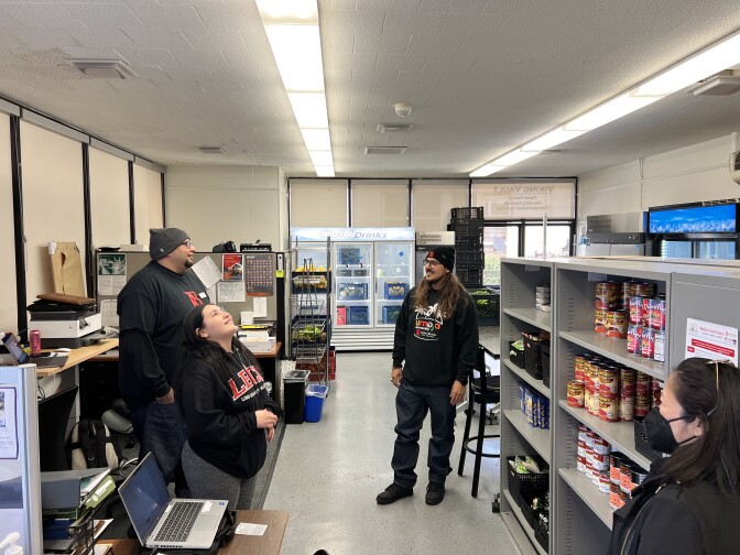 Two men and one young woman stand and laugh inside a food pantry, all wearing black LBCC sweatshirts.