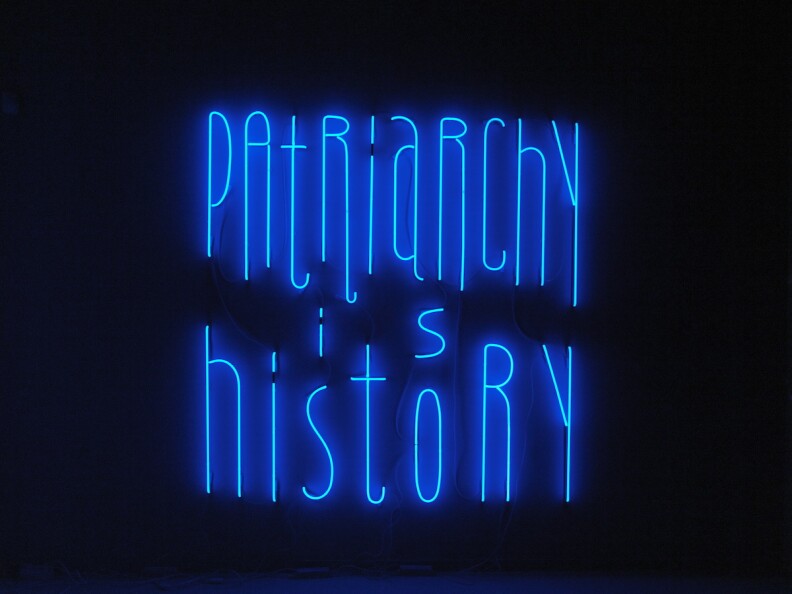 Blue neon letters on a black background read: "patriarchy is history"