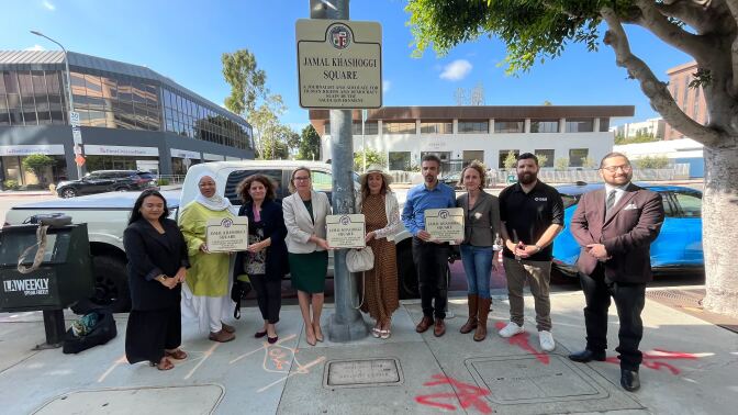 Nine people stand beside a street signed named Jamal Khashoggi Square. Cars and buildings are visible in the background.