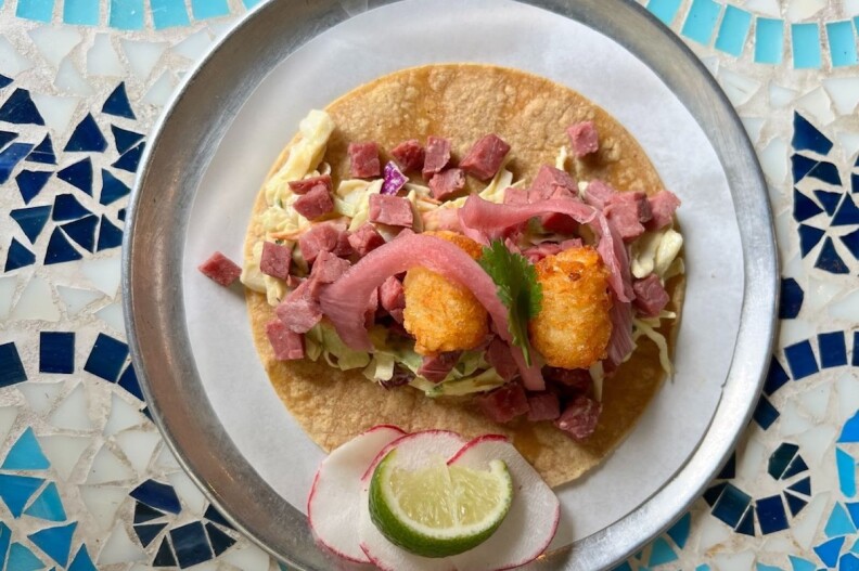 An open corned beef taco with a lime and radish slices at the bottom of the pic.