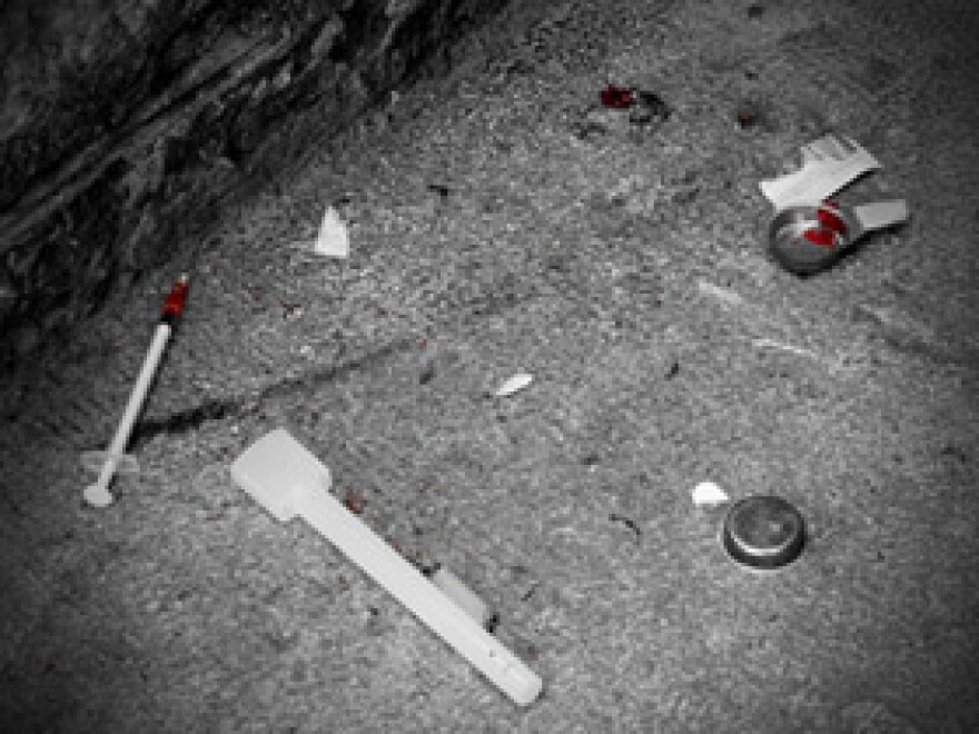 A dark picture of a street littered with a syringe and indictable paraphernalia.