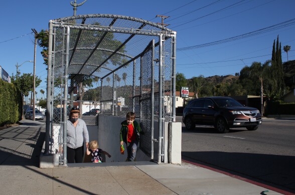A woman and her two children emerge from a set of stairs next to a road where a car drives by.