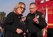 A woman wearing black listens to a man in uniform who is speaking to her and gesturing.