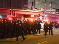 A group of LAPD officers wearing riot gear march toward protests in downtown L.A. near the federal detention facility on June 7, 2025. The police officers are carrying batons and marching in unison.