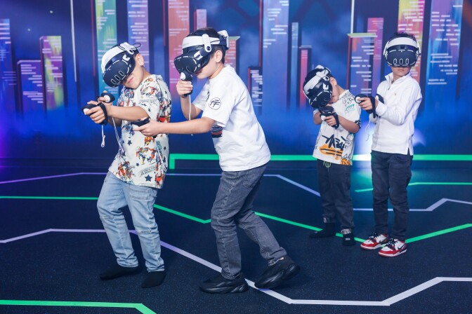 Children wear virtual reality headsets in a brightly colored room.