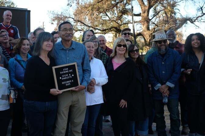 People pose for a photo. In front is a couple holding a sign.