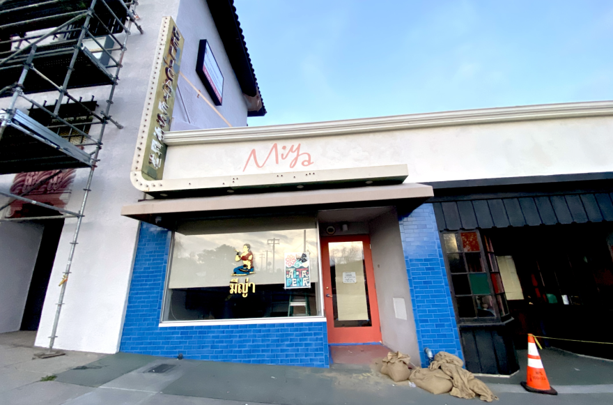 The exterior of a restaurant which says Miya above it. The front has bright blue tiles with a red painted door.