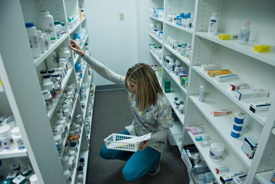 A person crouches down in a double-sided pharmacy isle to locate prescription medications.