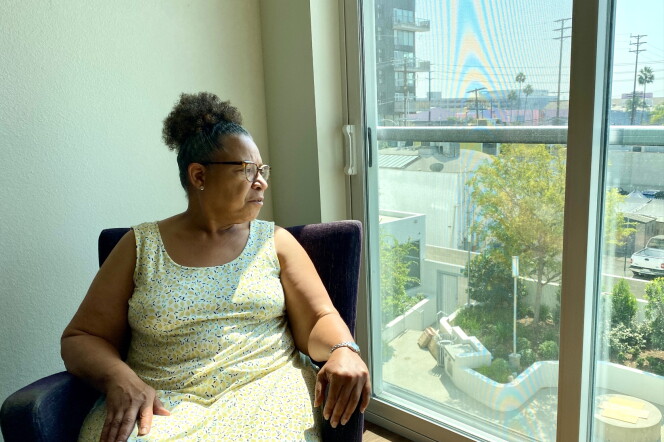 Lisa Chilton wears a flower sun dress while sitting in a chair in her living room while looking out the window.