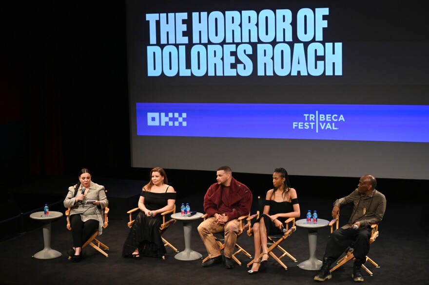 Five people sit on stage with a backdrop that says "The Horror of Dolores Roach."