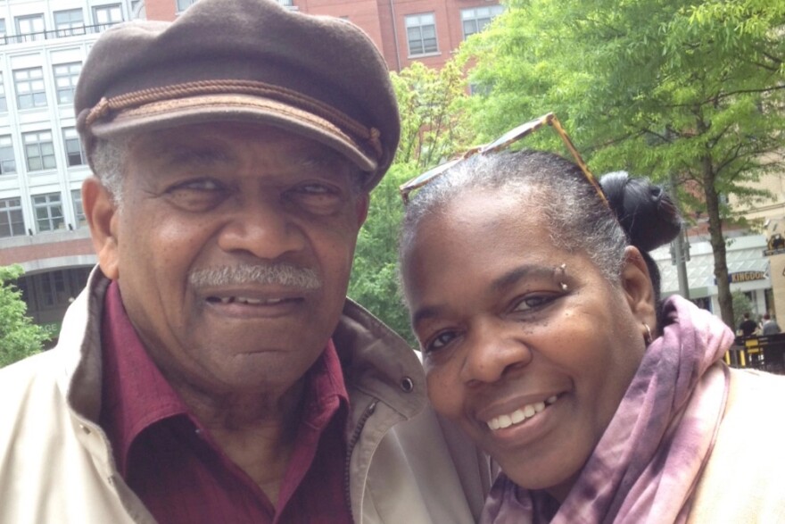 A man in a cap stands next to a woman in a scarf, both smile for a photo.