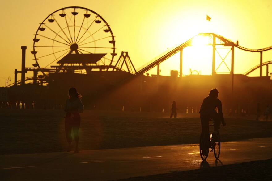A ferris wheel and a cyclist on a board walk as the sun sets in the background.