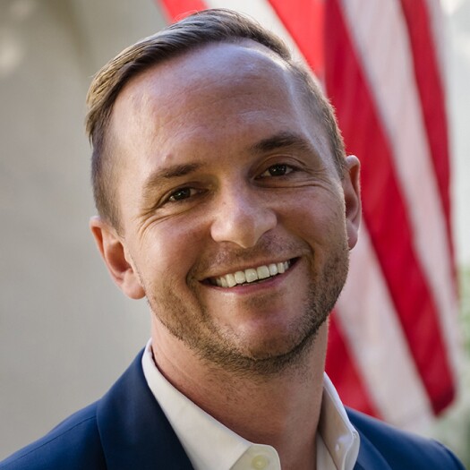 Headshot of Craig Greiwe. He's smiling and wearing a navy jacket and white collared shirt. He has a light complexion and short, blond hair cropped very close on the sides and combed to one side on the top.
