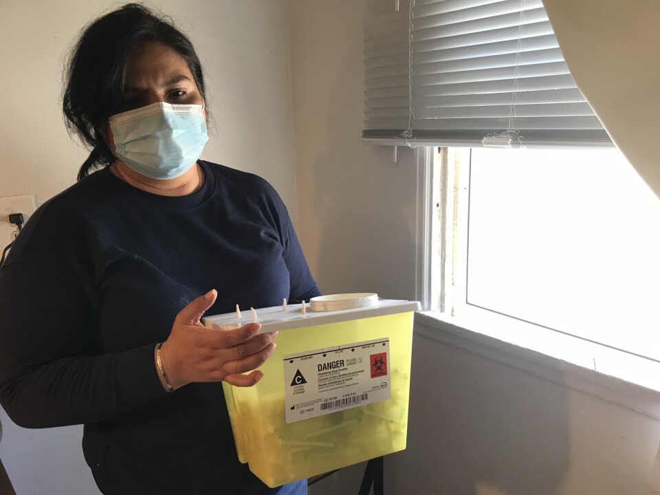 A woman holds a medical waste container holding used needles used to treat her daughter’s illness.