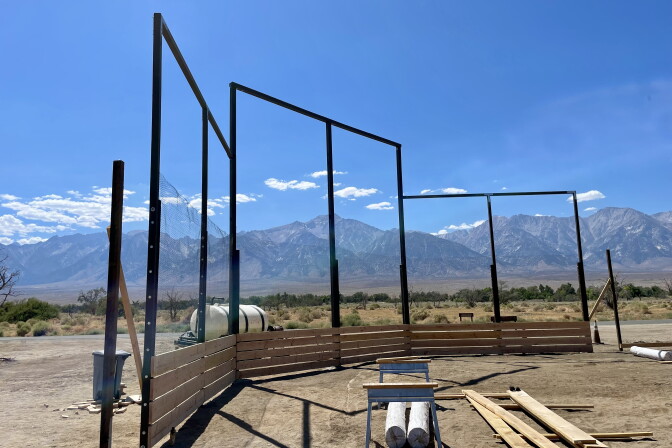 Wood lies on a dirt field with mountain peaks in the background.