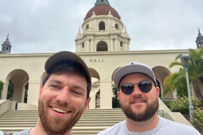 Two men, both wearing hats, post in front of the Pasadena City Hall