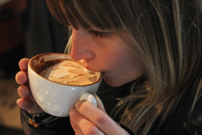 A young woman samples freshly-brewed cappuccino. A growing number of so-called third wave artisinal coffee bean roasters are finding a niche market in Europe and the USA for their carefully-crafted and expensive coffee.