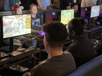 A group of people sitting in front of monitors and playing Street Fighter 6.