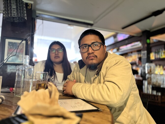 A Latina fan (l.) and Latino fan (r.) watch a screen off-camera.