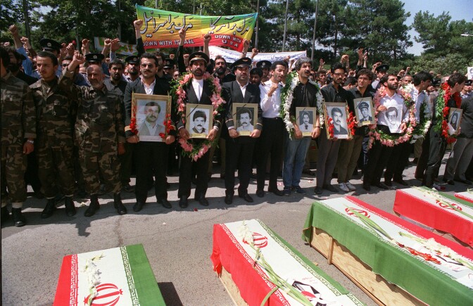 People holding pictures stand in a line in front of coffins.