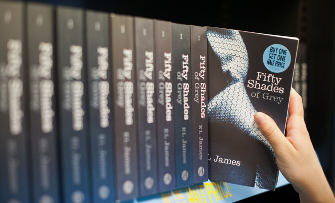 A woman takes a copy of the novel 'Fifty Shades of Grey' from a shelf.