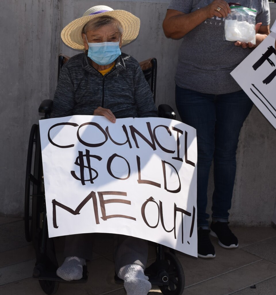 Older woman holds a protest sign saying "council sold me out"