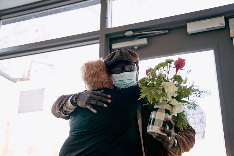 A woman and a man hug while the man holds a flower bouquet.