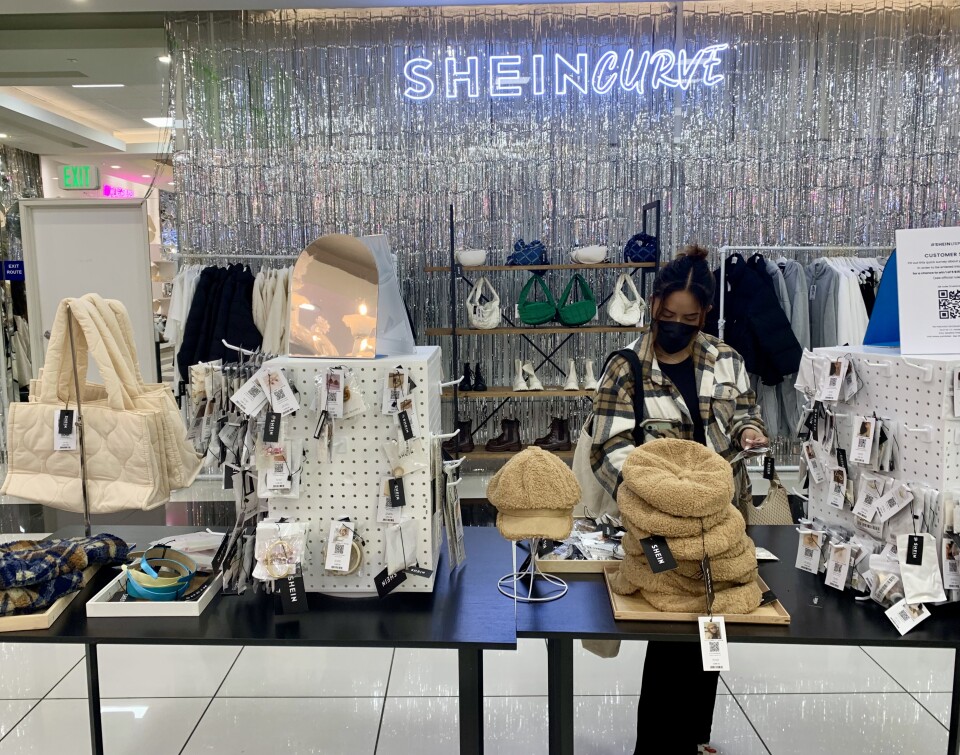 A woman in a mask browses a table of Shein accessories at a recent pop-up, including purses, jewelry and hats. 