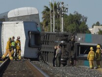 Firefighters and other officials walk near cars from a Metrolink passenger train that derailed Tuesday, Feb. 24, 2015, in Oxnard, Calif. Three cars of the Metrolink train tumbled onto their sides, injuring dozens of people in the town 65 miles northwest of Los Angeles.