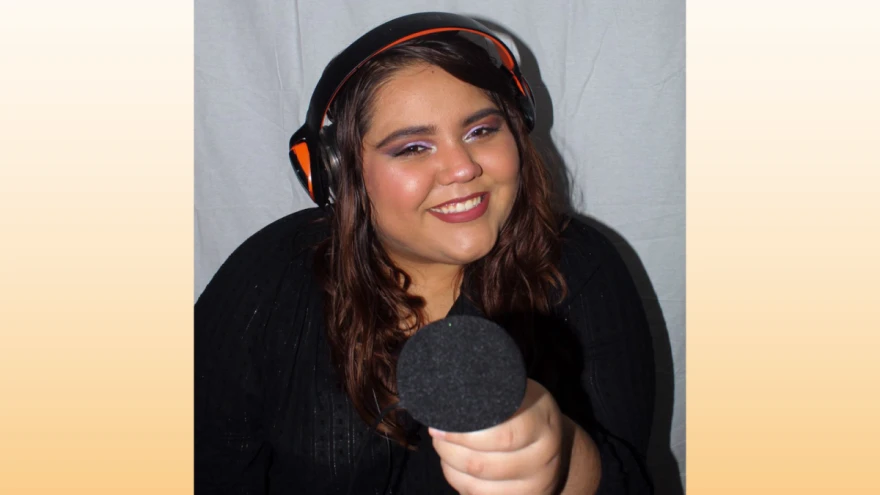 Carmen González, a woman with medium skin tone wearing a black long sleeve shirt, smiles as she wears headphones and points a microphone to the camera.