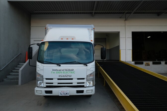A white Isuzu medium-duty truck outside a warehouse. 