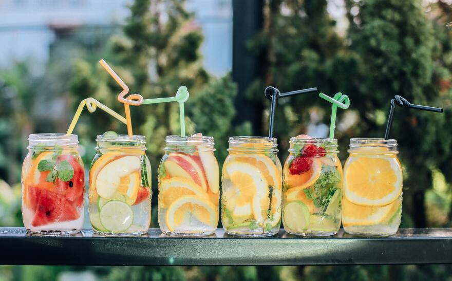 a variety of fruit-filled cocktails in clear glasses with twisty straws