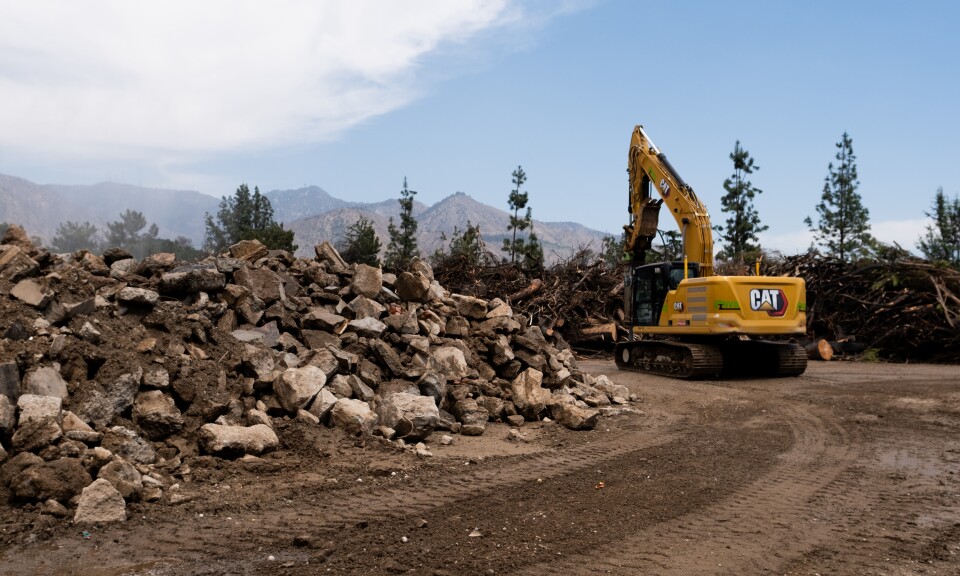 A big machine and piles of concrete with wood in the background.
