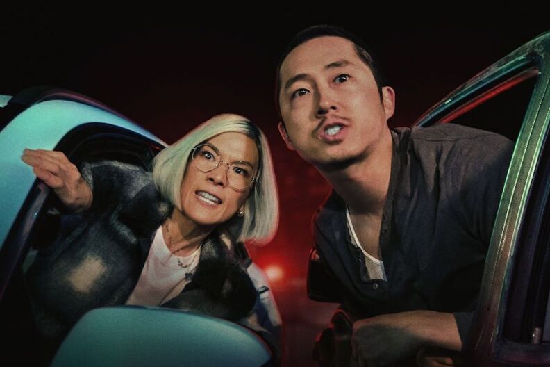 Ali Wong and Steven Yeun lean out of their respective car windows, toward each other, while about to yell at who or what's in front of them.