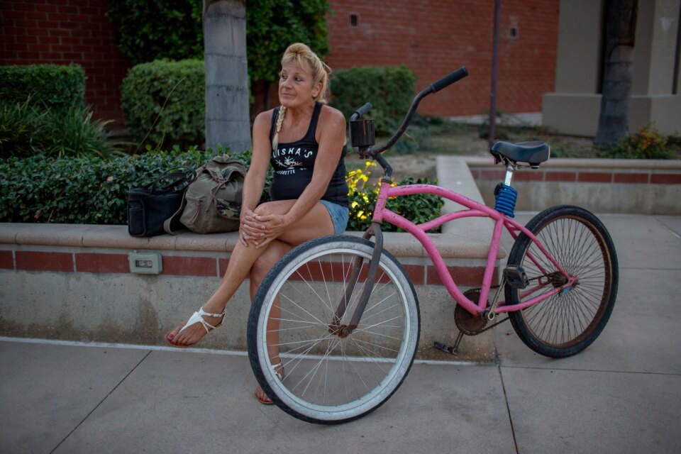 A woman sits on a ledge with her bike and bags.