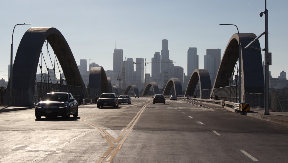 Cars travel both directions of the bridge with looping arches on either side and a view straight to the skyscrapers of downtown L.A.