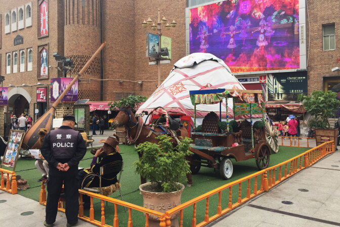 At Urumqi's Grand Bazaar, a police officer chats with a local vendor while a video promoting China's ethnic minorities plays on a big screen overlooking the square. This was the site of Uighur protests in 2009 that sparked citywide riots, leading to the death of hundreds. Since then, the city has become one of China's most tightly controlled police states.
