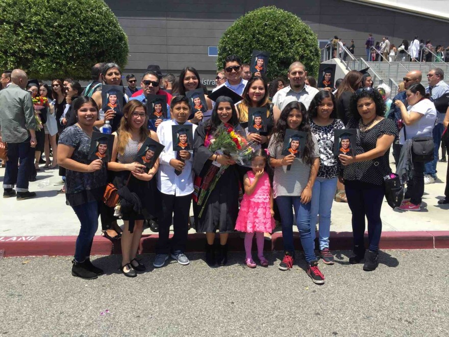 A woman in a black cap and gown holding flowers poses in a picture with her family at her graduation from University of La Verne in La Verne, CA.