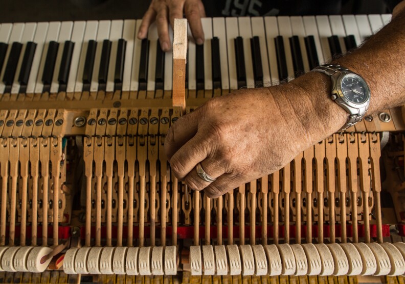 Enrique Beruman, a piano repair technician, tests the action on a piano keyboard.