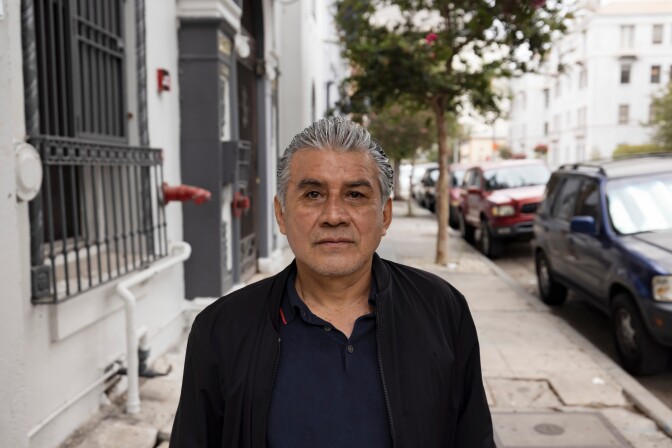 A photo of Eduardo Jarquin photographed outside an apartment building in Koreatown. He is wearing dark clothing.