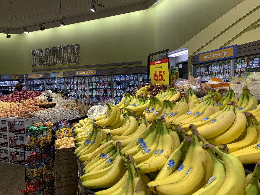 A produce section of a market has a large display of bananas in the foreground.